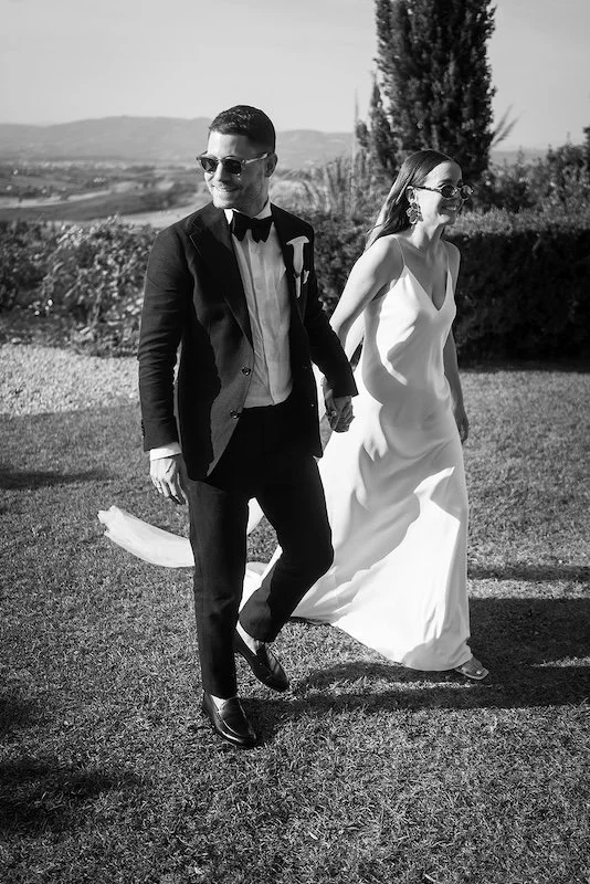Brautpaar im klassischen Schwarz-Weiß-Stil, Hand in Hand durch die malerische Umgebung des Gardasees - stilvolle Hochzeitsfotografie in Italien.