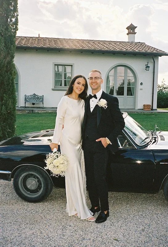 Brautpaar posiert elegant neben einem Oldtimer vor einer toskanischen Villa