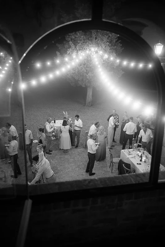 Wedding guests at night under strings of lights in the courtyard of Villa Boscarello