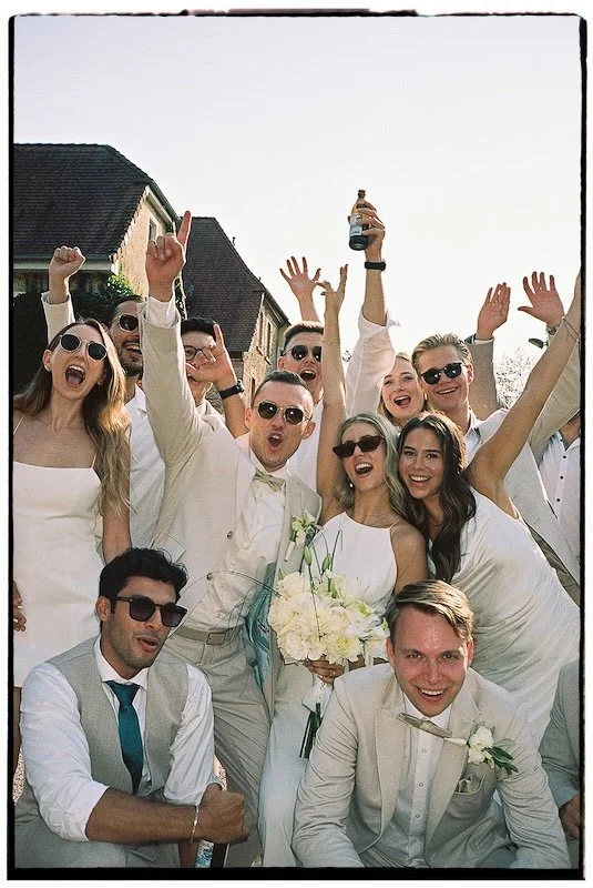 Analoges Bild mit Rahmen von einer ausgelassene Gruppe von Gästen jubelt und lacht in die Kamera während der Hochzeit im Hofgut Nonnenau