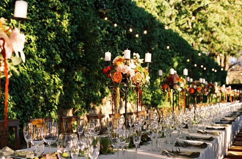 A set wedding table with candles and flowers in front of a wall of ivy, photographed on film