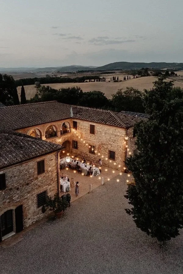 Abendliche Hochzeitstafel im Innenhof der Villa Boscarello mit Lichterketten, dahinter die Hügel des Val d'Orcia