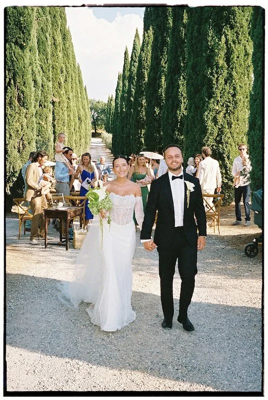 After the wedding ceremony, the bride and groom walk down the cypress-lined avenue at Villa Boscarello; analog photograph