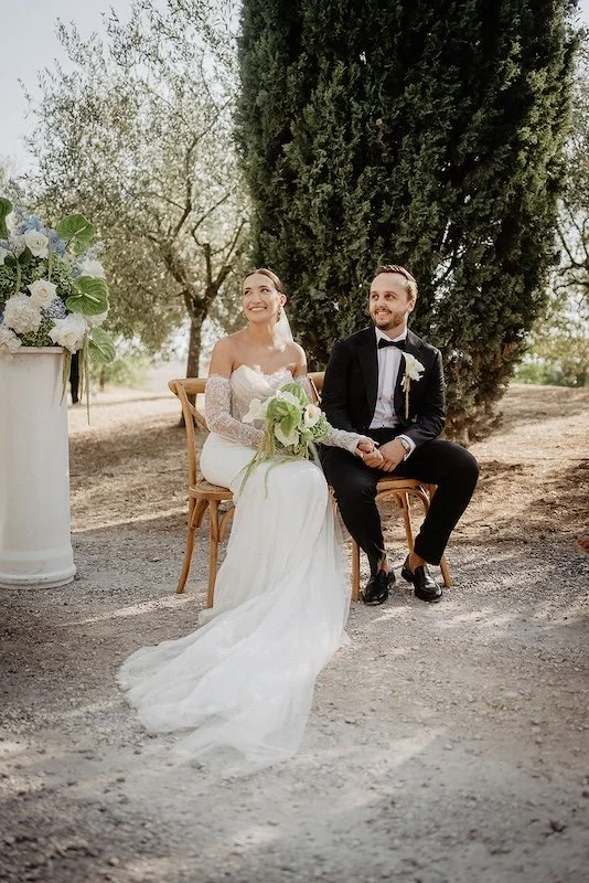 The bride and groom sit in the olive grove at Villa Boscarello during the outdoor wedding ceremony