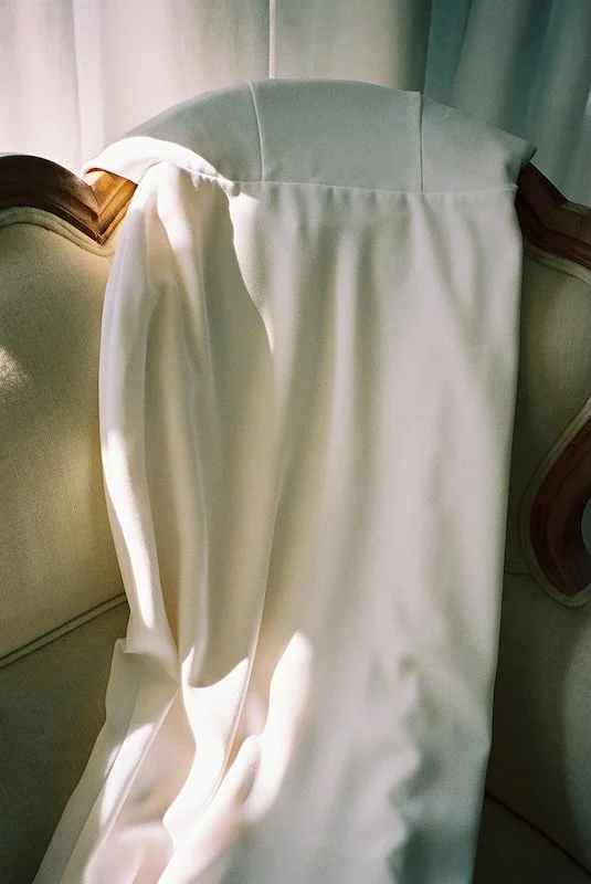 Detailaufnahme eines Brautkleides, das im warmen Licht über einem Stuhl hängt