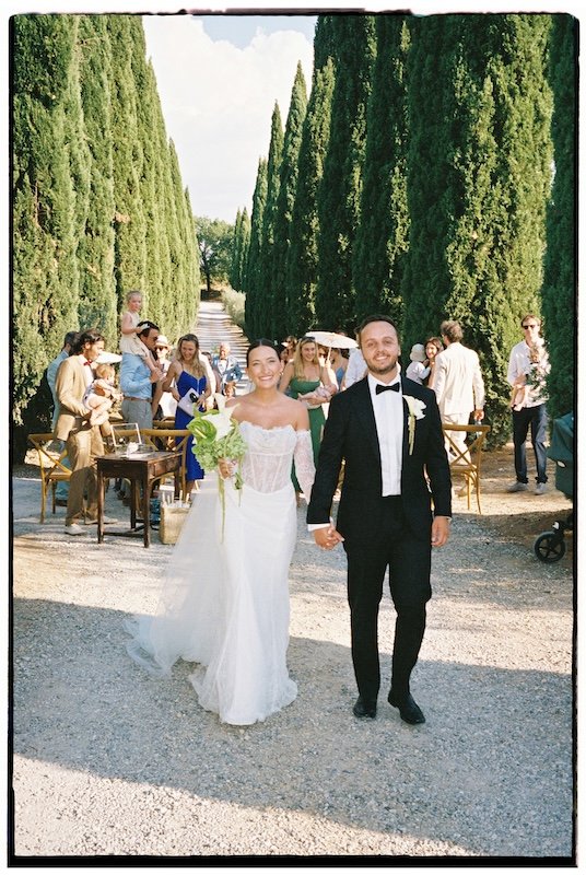Analoge Aufnahme auf einem Portra 400 35mm Film eines Brautpaar mit seinen Gästen zwischen den Zypressen bei einer Hochzeit in der Villa Boscarello in der Toskana