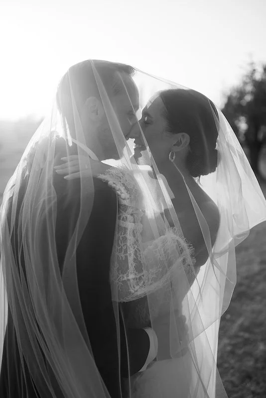 The bride and groom under the veil, backlit, at their wedding at Villa Boscarello