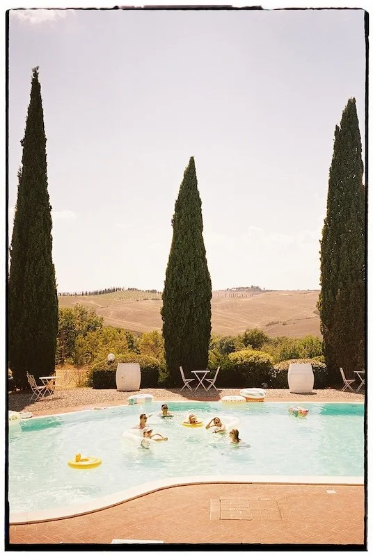 Guests are swimming with swim rings in the pool at Villa Boscarello, with cypress trees and the Tuscan hills in the background