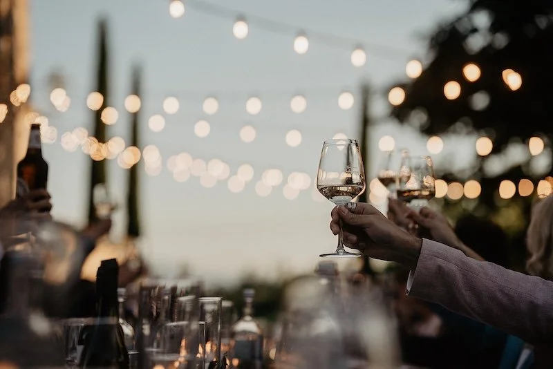 Guests raising their glasses during an outdoor wedding dinner beneath string lights at a Tuscan villa.