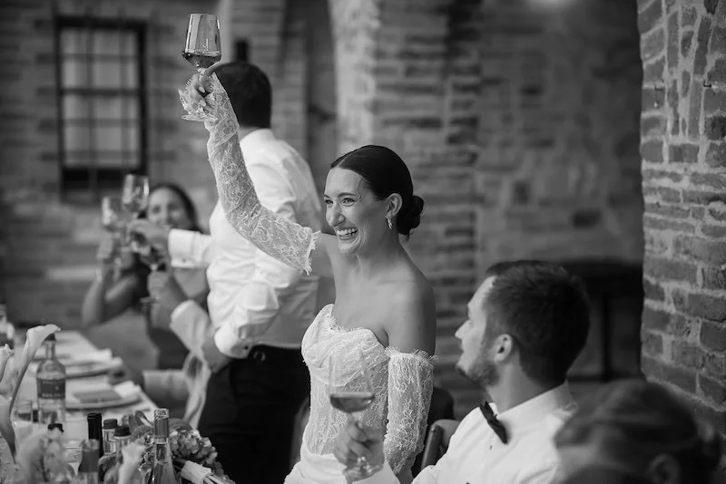 The bride raises her glass with a laugh during the wedding dinner at Villa Boscarello
