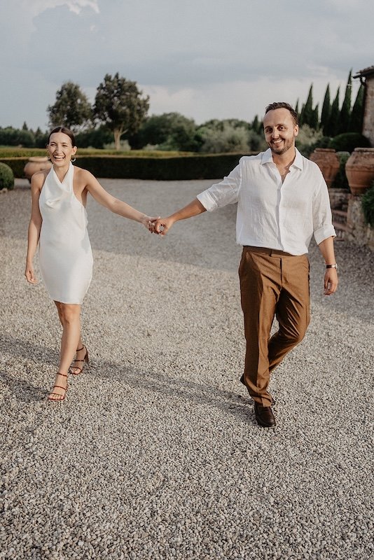 The bride and groom, dressed casually, walking hand in hand along the gravel path at Villa Boscarello