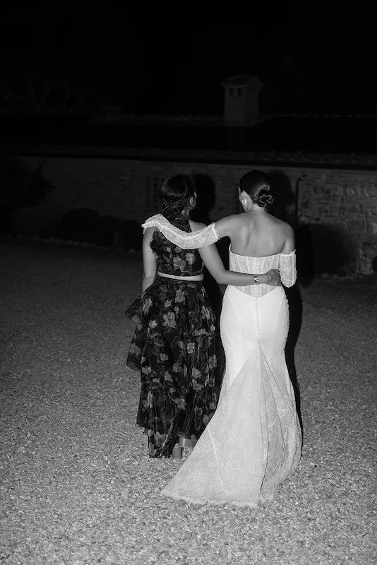 The bride and a guest walk along the gravel path at Villa Boscarello at night; black-and-white photograph