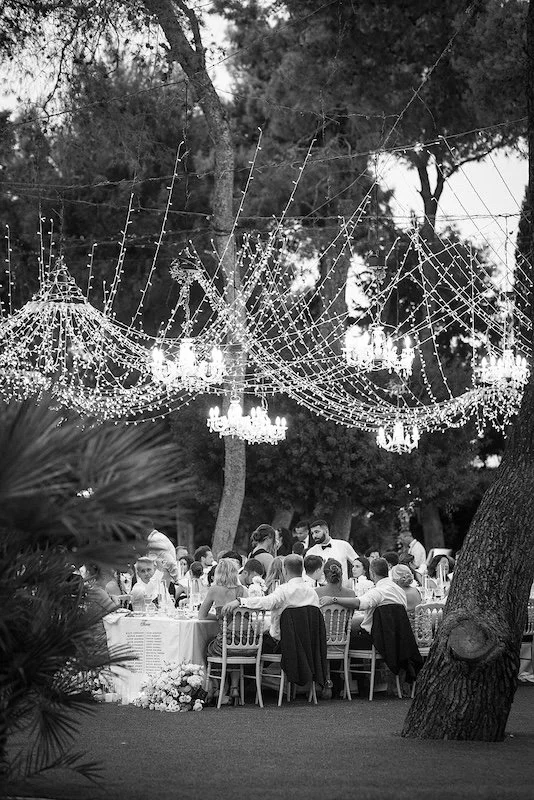 Hochzeitsdinner unter Pinien mit Lichterketten und Kronleuchtern in Castello Monaci