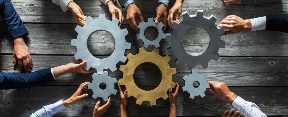 Multiple hands positioning interconnected gears on a table, representing coordinated IT support and collaboration.