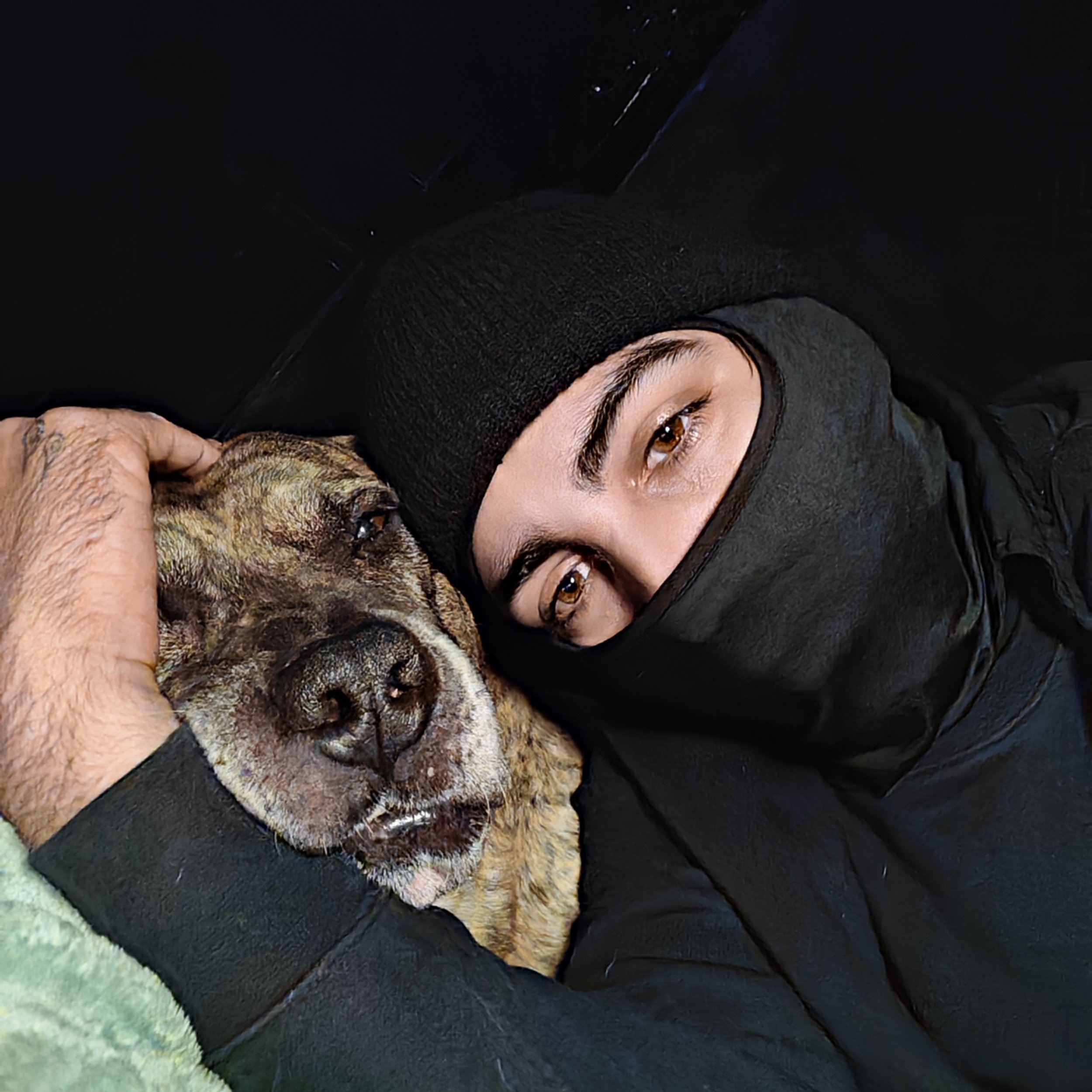 A person in a black ski mask and coat lying down with their head next to a dog, both with eyes closed, appearing to rest or sleep together.