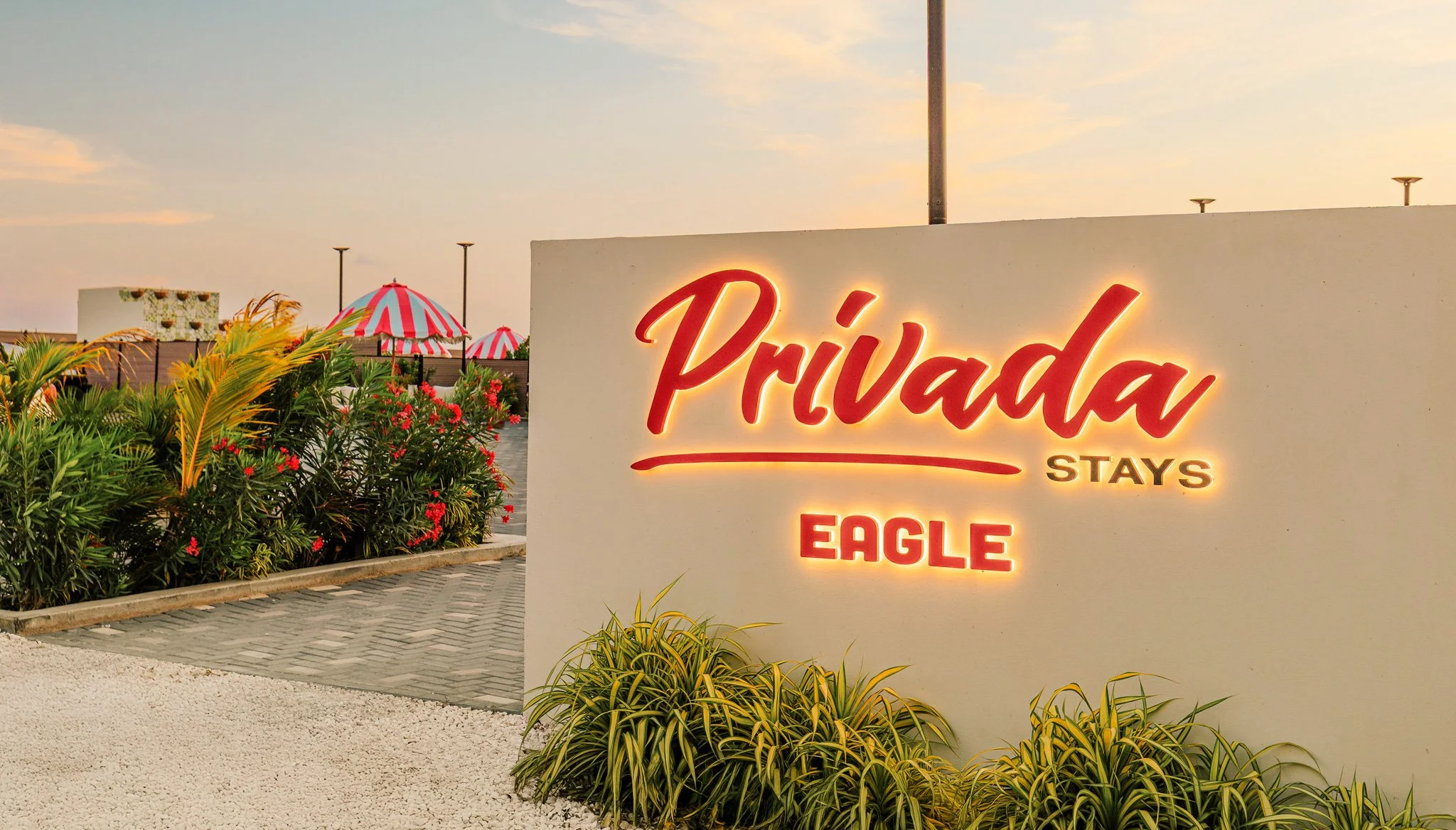 Sign that reads 'Privada stays eagle' with plants and umbrellas in the background at sunset.