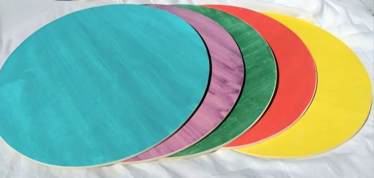 Fünf bunte runde Papierkreise in Blau, Lila, Grün, Rot und Gelb, übereinander auf weißem Stoff