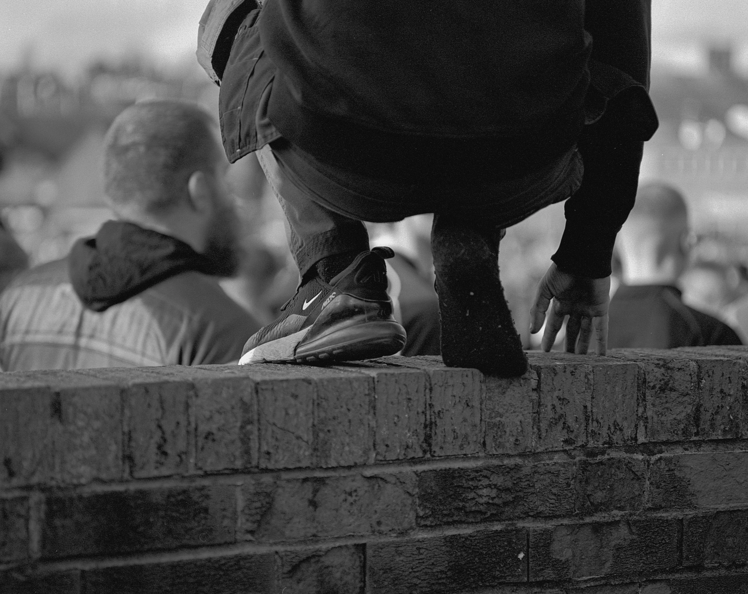 A person in sneakers, with one missing balances on a brick wall while reaching down.