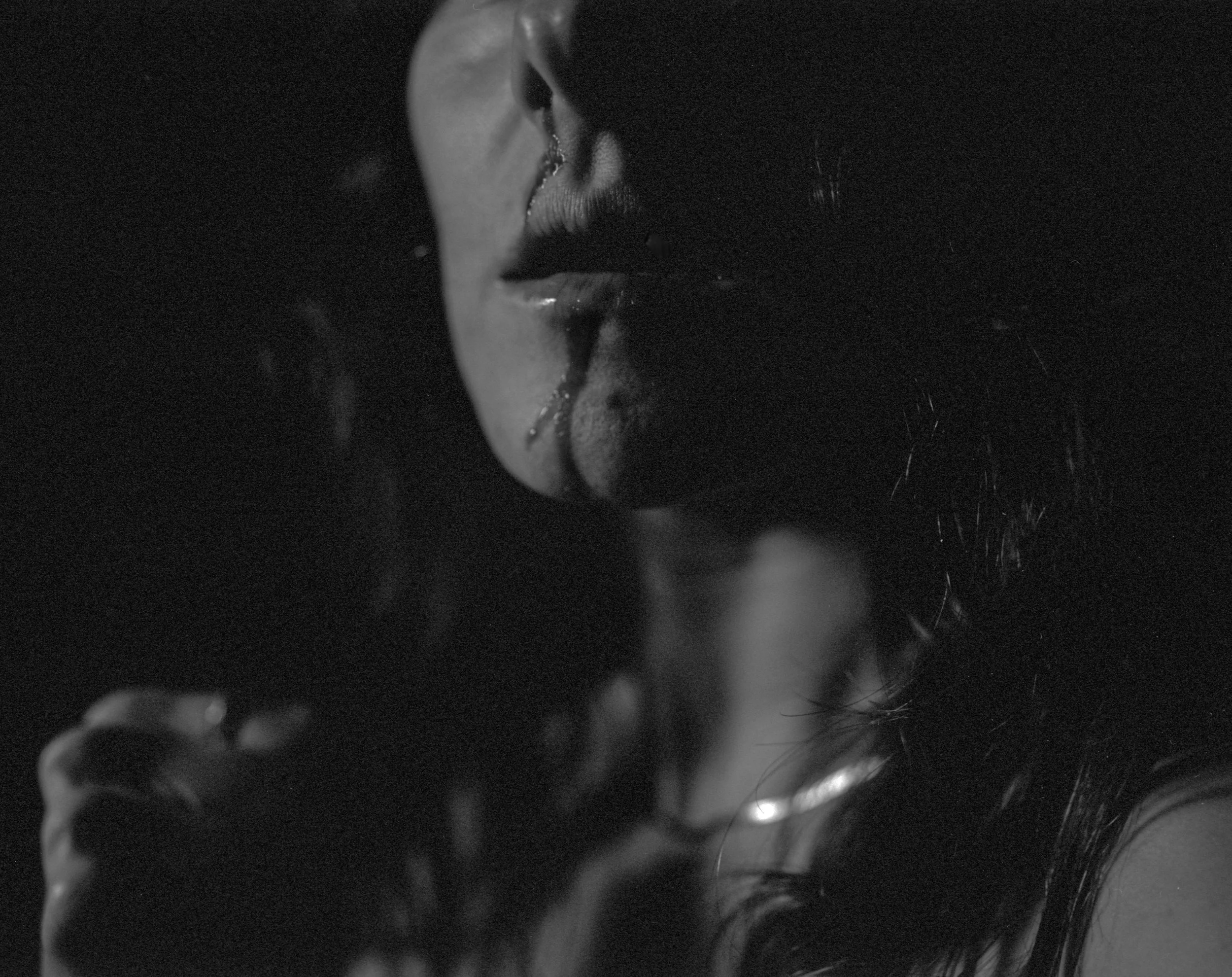Close-up black and white photo of a woman with dark hair, lips slightly parted, with a drop of liquid on her lower lip.