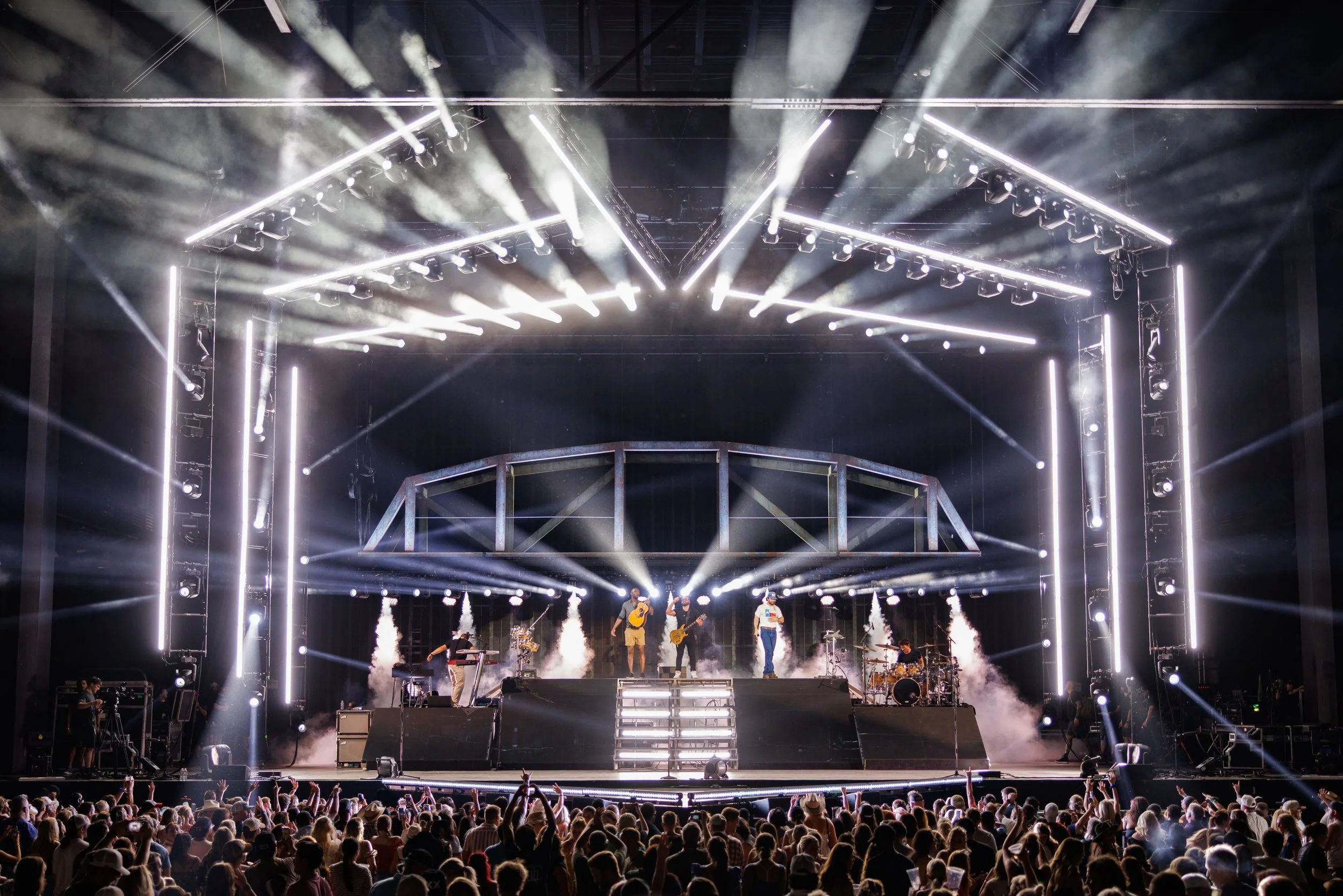 A concert stage with bright lights, smoke effects, and a band performing in front of a large audience.