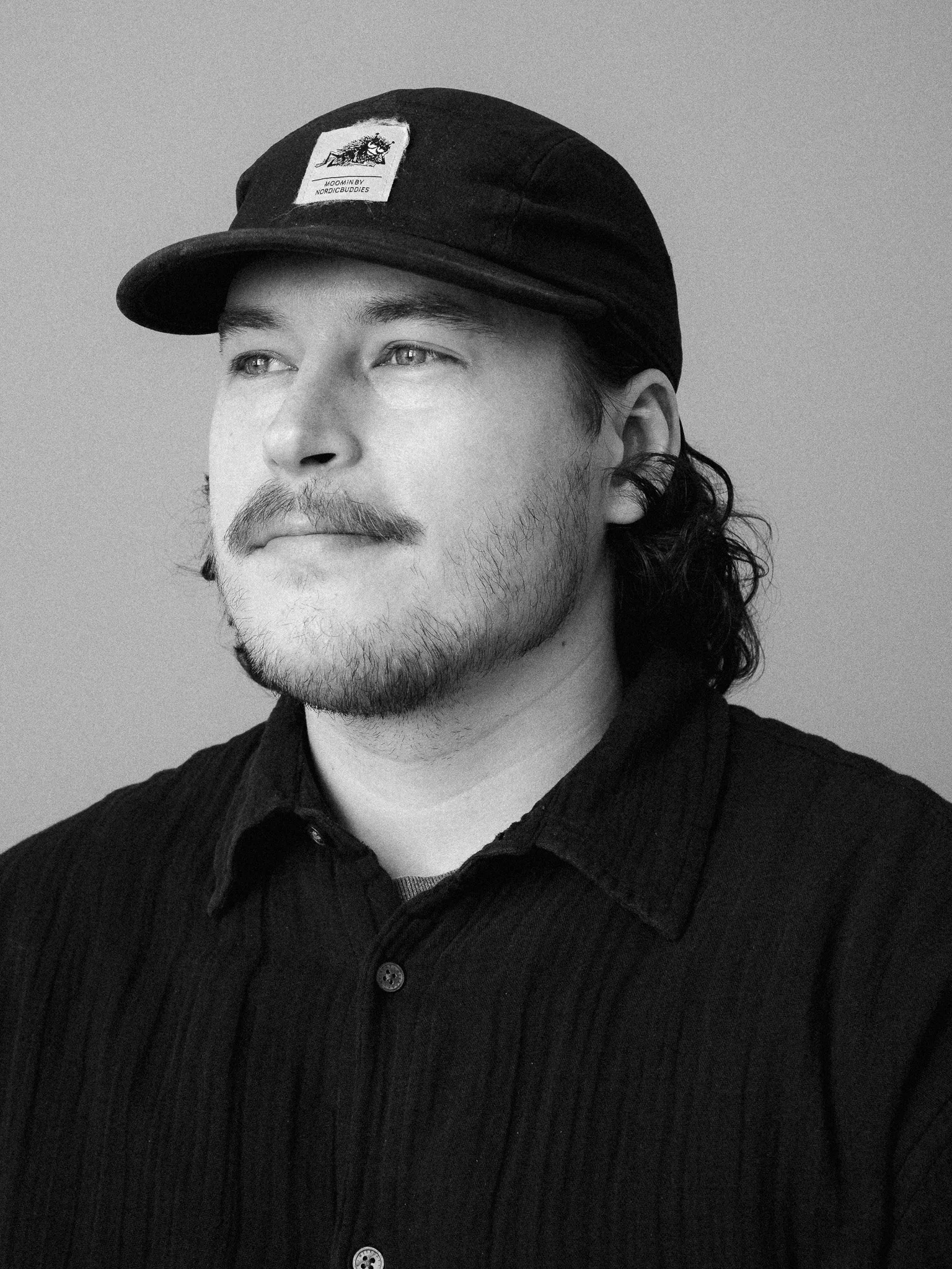 Black and white portrait of a man with slicked-back hair and a beard, wearing a dark button-up shirt, looking off to the side.