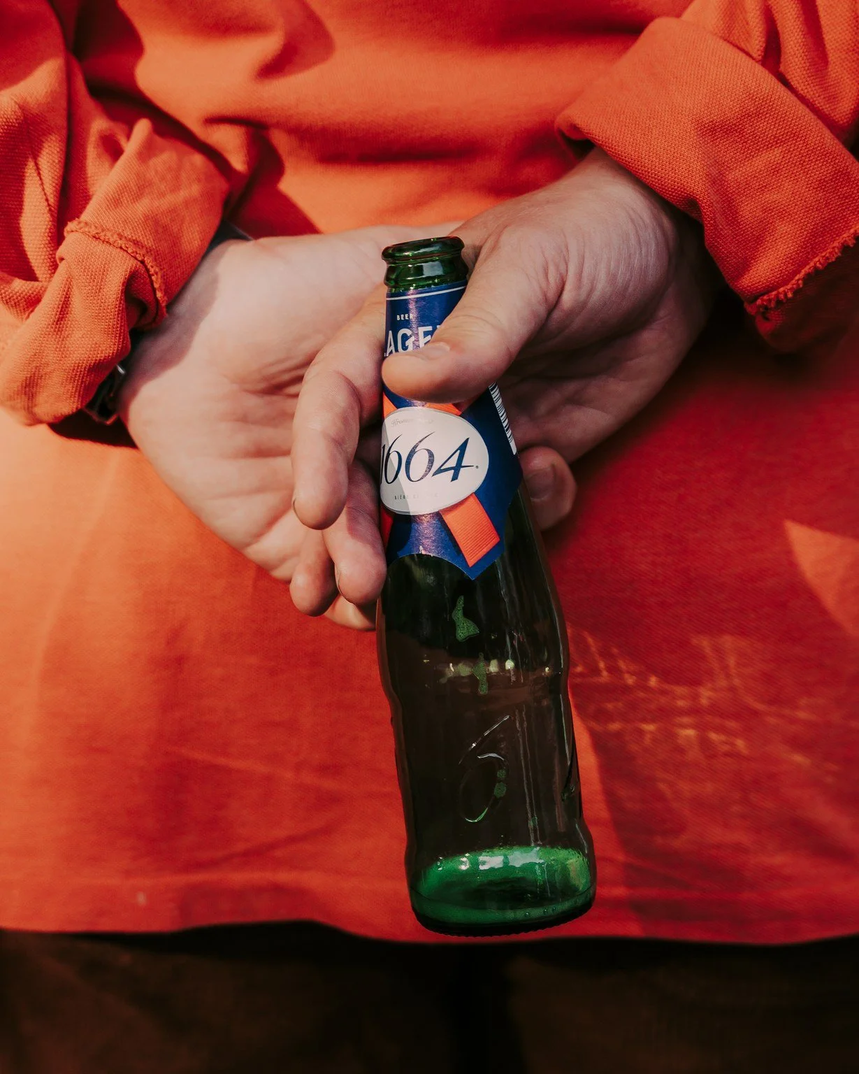 A person holding a glass bottle of beer with a green tint, wearing an orange shirt.