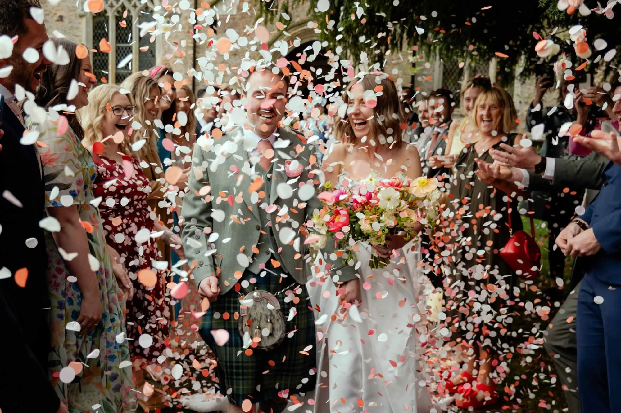 A wedding celebration with a bride and groom holding hands surrounded by friends, as colorful confetti falls around them.