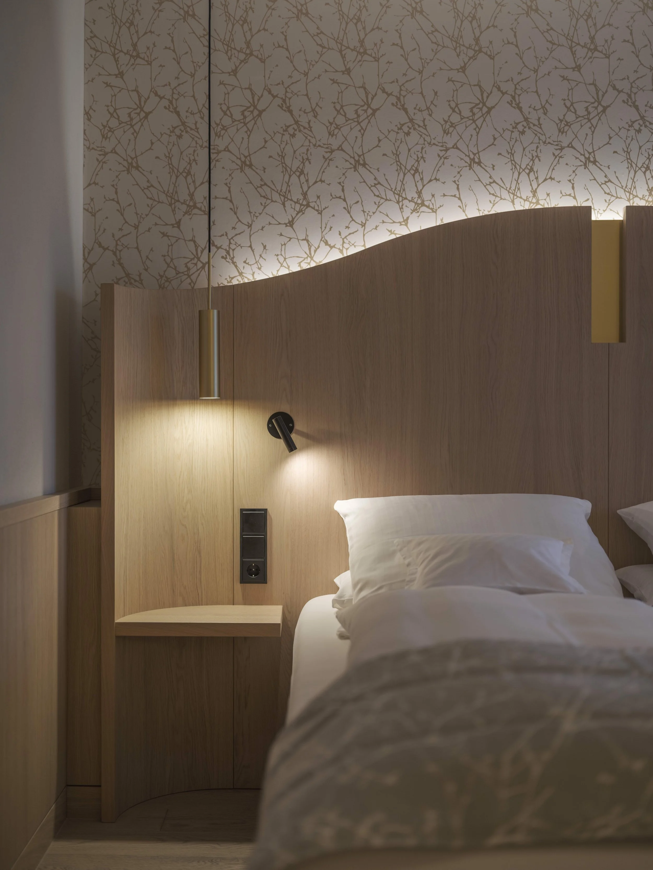 Ein modernes Schlafzimmer mit einem Bett, einem Holzkopfteil, einer Leselampe und einem dekorativen Tapetenhintergrund.