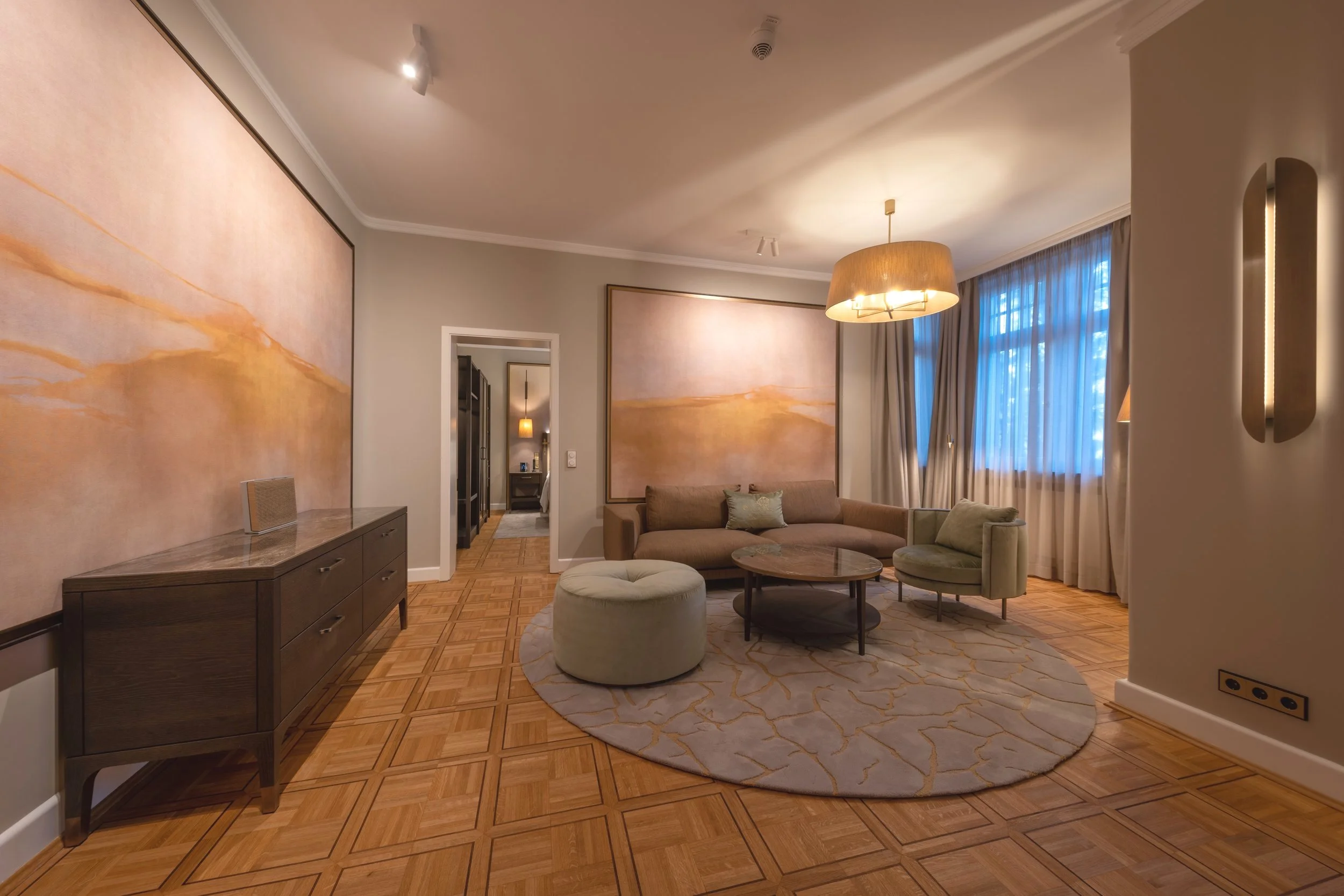 Gemütliches Wohnzimmer mit moderner Einrichtung, Sofa, Sesseln, Teppich und großer Wandkunst.