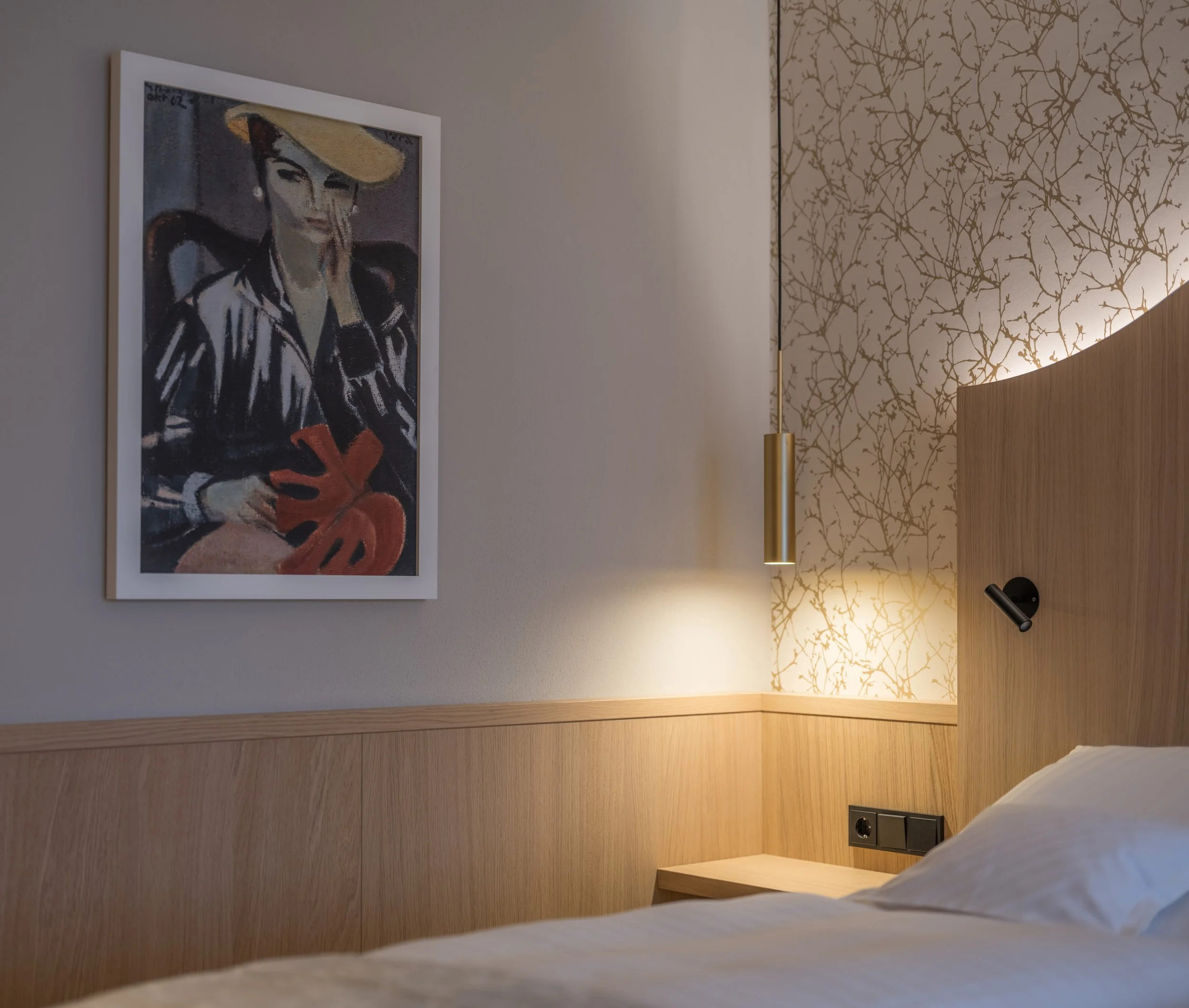 Ein eingerichtetes Schlafzimmer mit einem Bett, einer Holzwand und einem Rahmen mit Wandlampen. An der Wand hängt ein Gemälde einer stilisierten Frau mit Hut, die eine rote Pflanze hält.