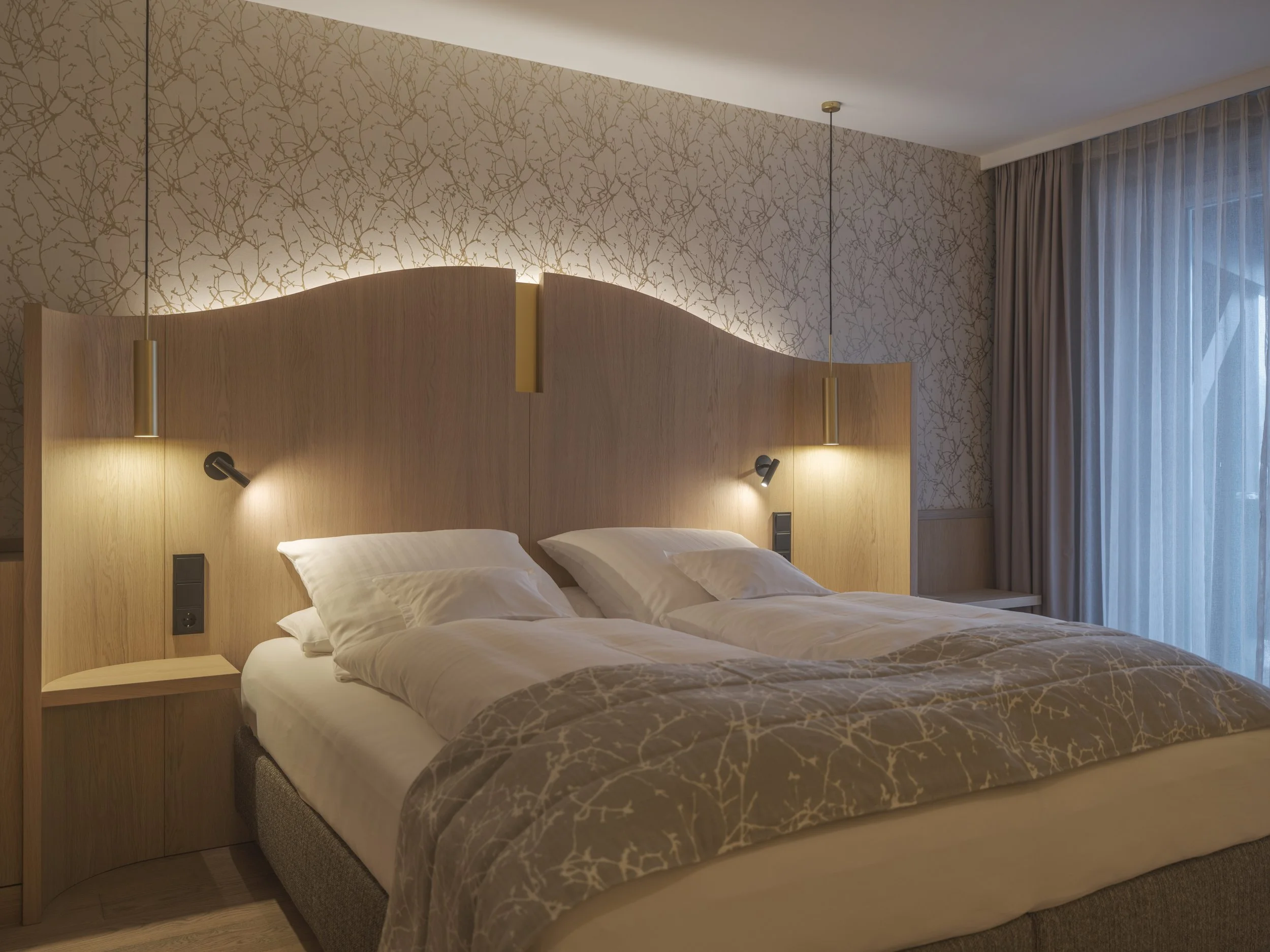 Ein Schlafzimmer mit Doppelbett, zwei Nachttischen, Wandlampen und Vorhängen vor einem Fenster.