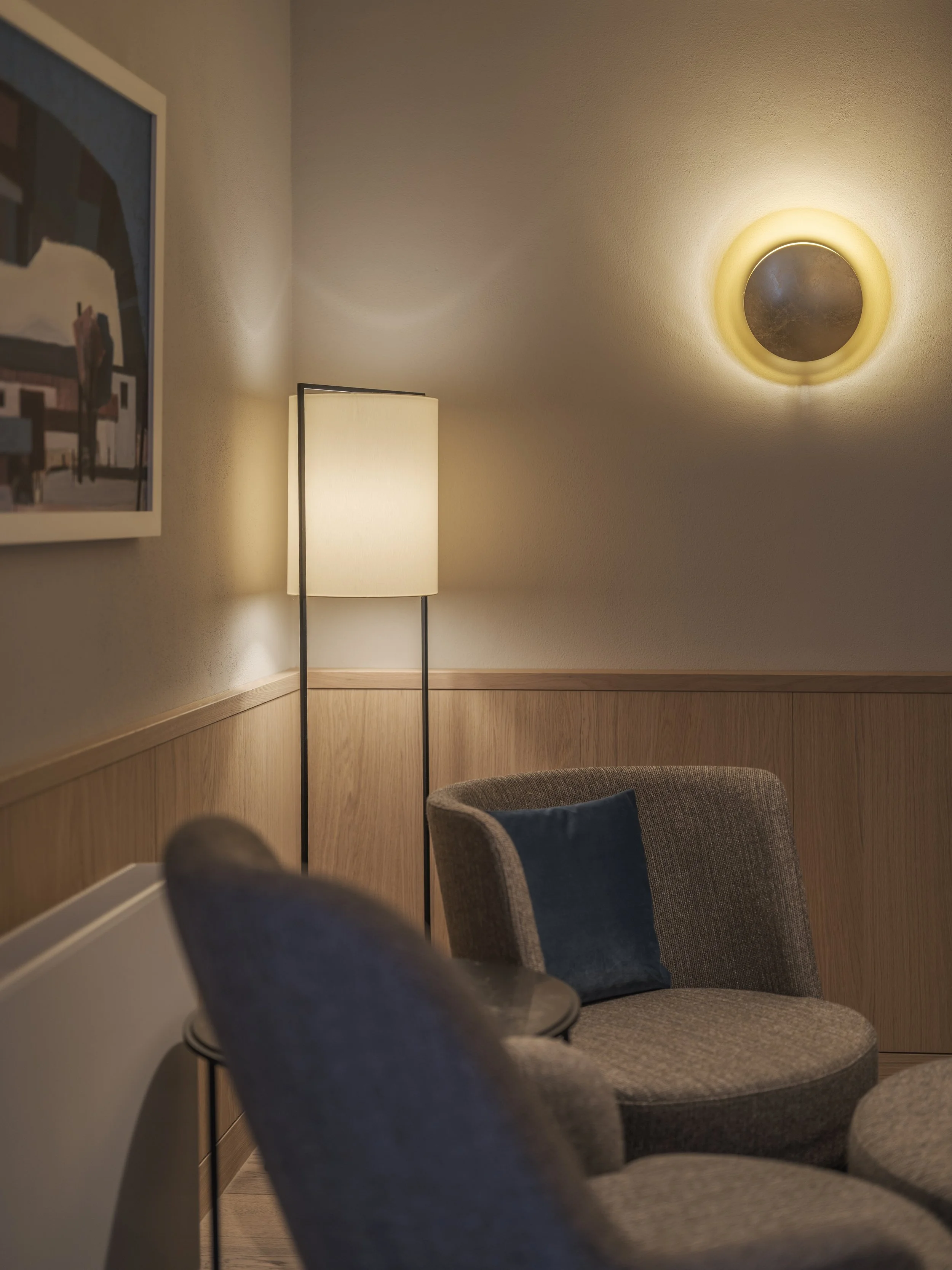 Gemütliches Wohnzimmer mit Stehlampe, einem runden Sessel mit Kissen, Wandlampe und Wandbild.