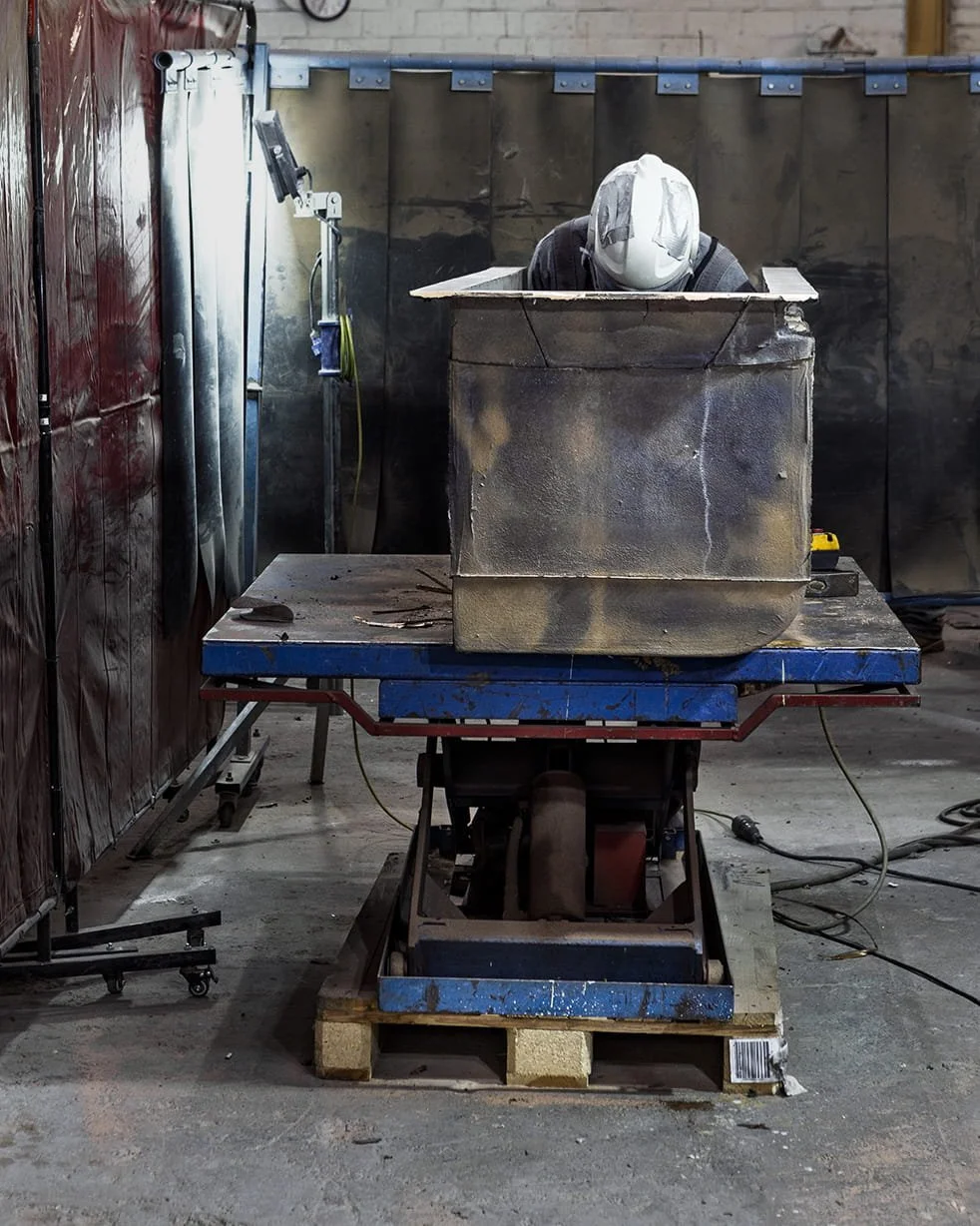 Schweißer mit Schutzhelm arbeitet an einem großen Metallbehälter in einer Werkstatt.