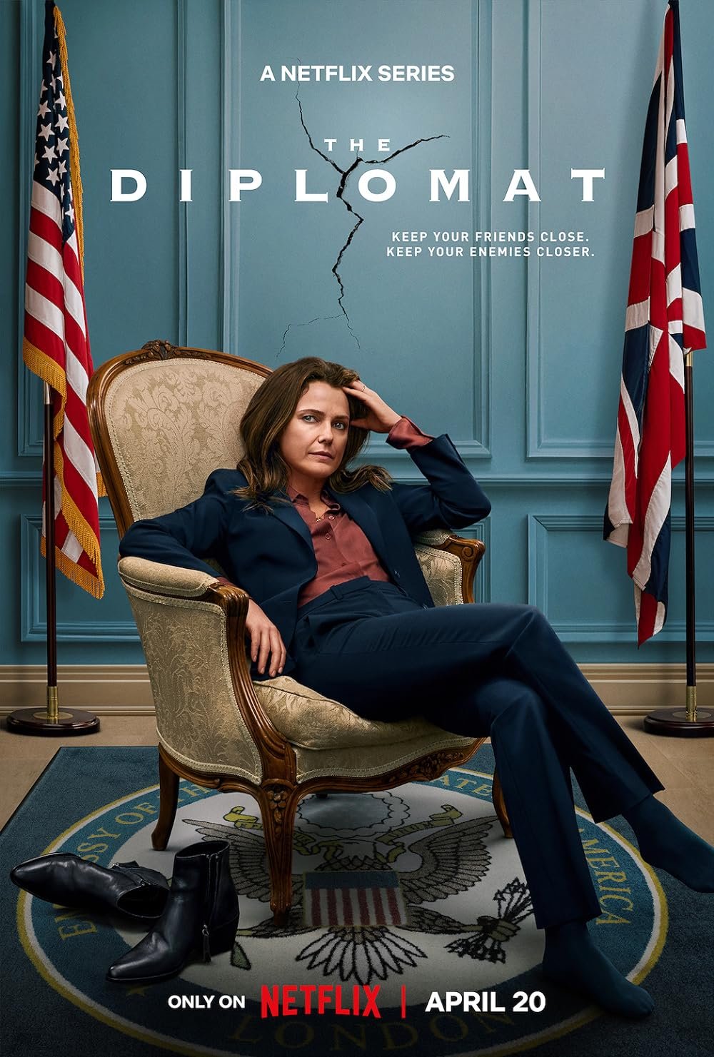 Poster for the Netflix series 'The Diplomat' featuring a woman sitting on a chair, with flags of the United States and the United Kingdom behind her, and a cracked wall in the background. The woman appears serious and confident, with her shoes off on