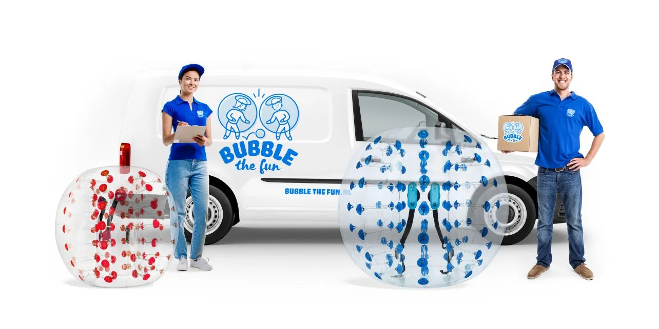 Man en vrouw in blauwe uniforms staan voor een witte bedrijfswagen met logo 'BUBBLE the fun'. De vrouw houdt een clipboard en de man houdt een doos. Er liggen twee grote doorzichtige ballen met plastic stippen, een rode en een blauwe.