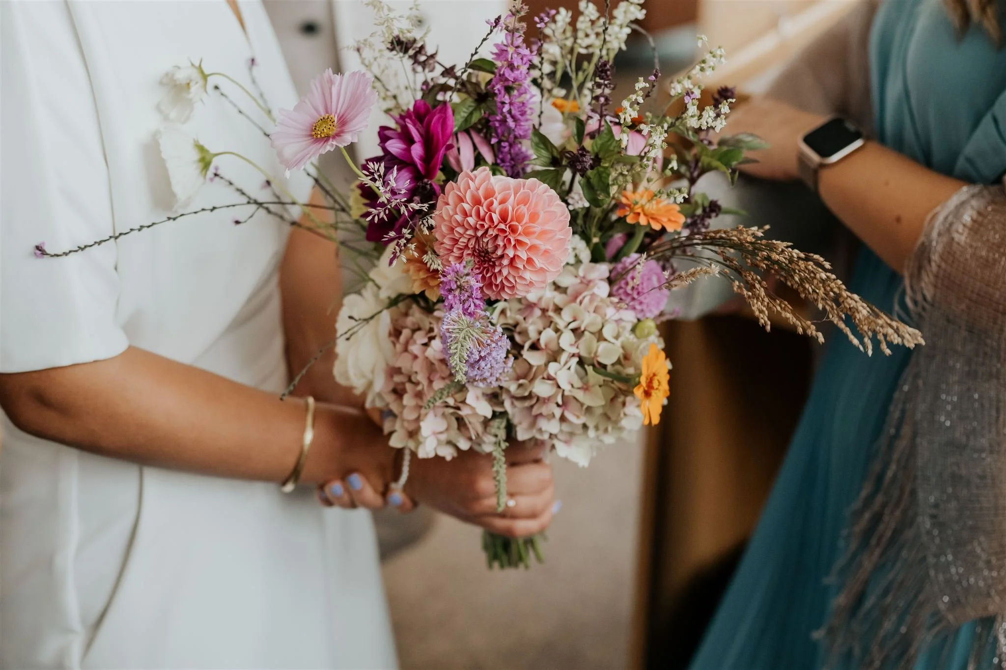 Una persona tiene un bouquet di fiori color pastello, tra cui dahlia, gigli e rose, tenuto con entrambe le mani.