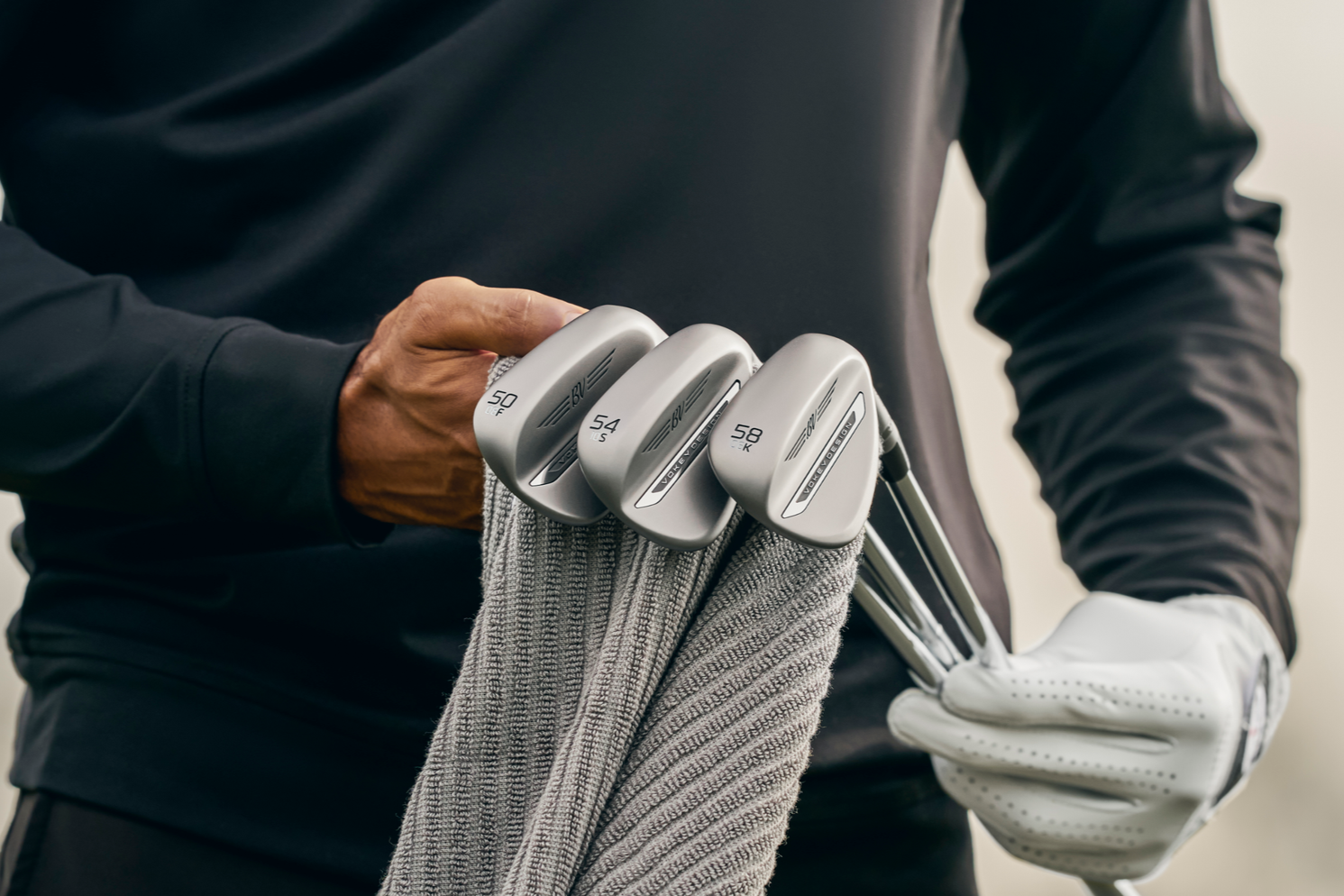 Person som håller ett urval av golfklubbor med nummer 52, 56, 60 och 64