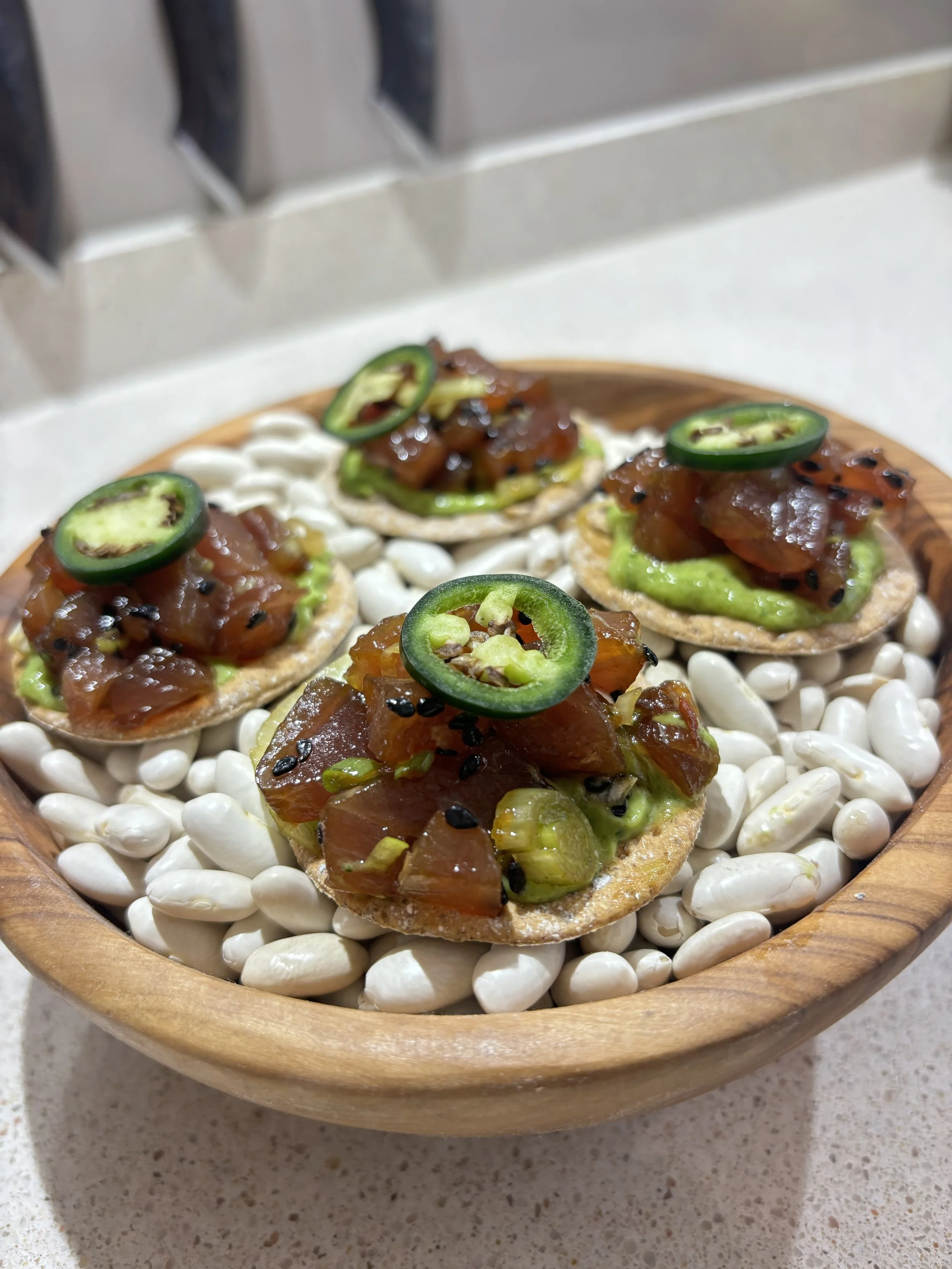 Asian-Inspired Tuna Tostada  Marinated tuna tartare layered over avocado purée on crisp tostadas, finished with fresh jalapeño, black sesame, and citrus-soy vinaigrette.