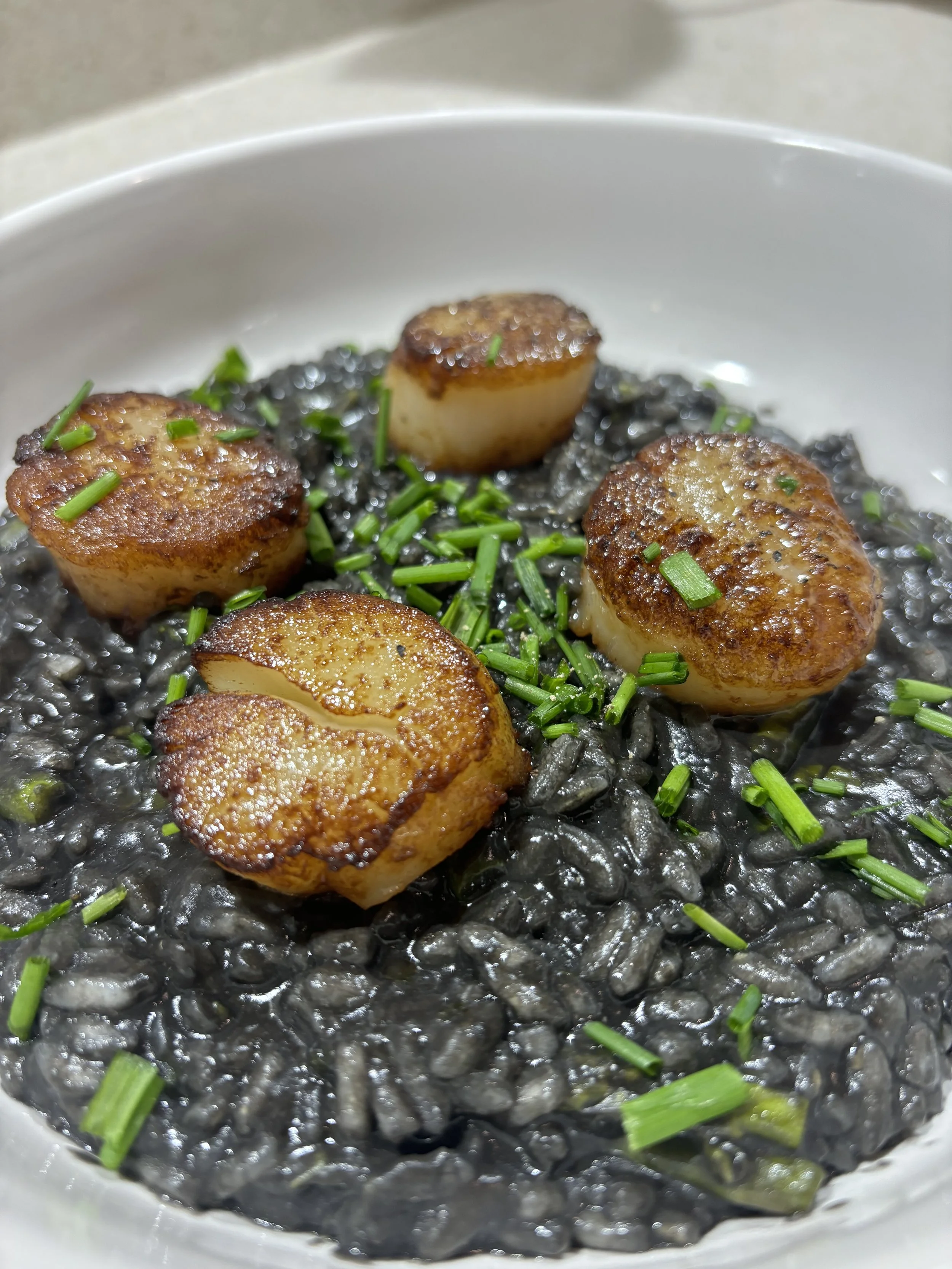 Glazed Scallops with Squid Ink Risotto  
Pan-seared sea scallops finished with a hot honey glaze, served over squid ink risotto, garnished with fresh chives, and finished with extra-virgin olive oil.