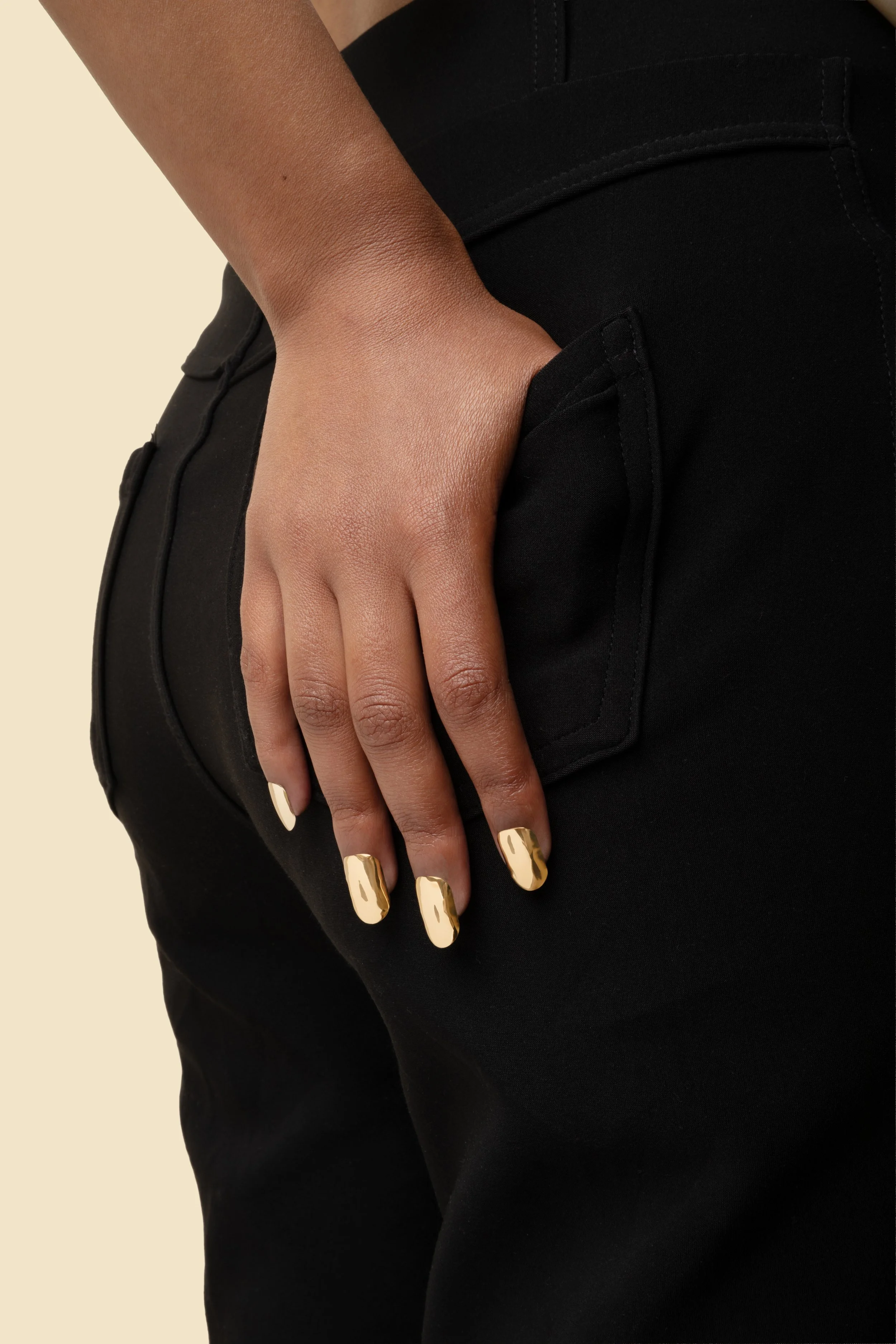 Hand on hip wearing 14k gold press-on nails by Stey Gold with gold rings and black clothing