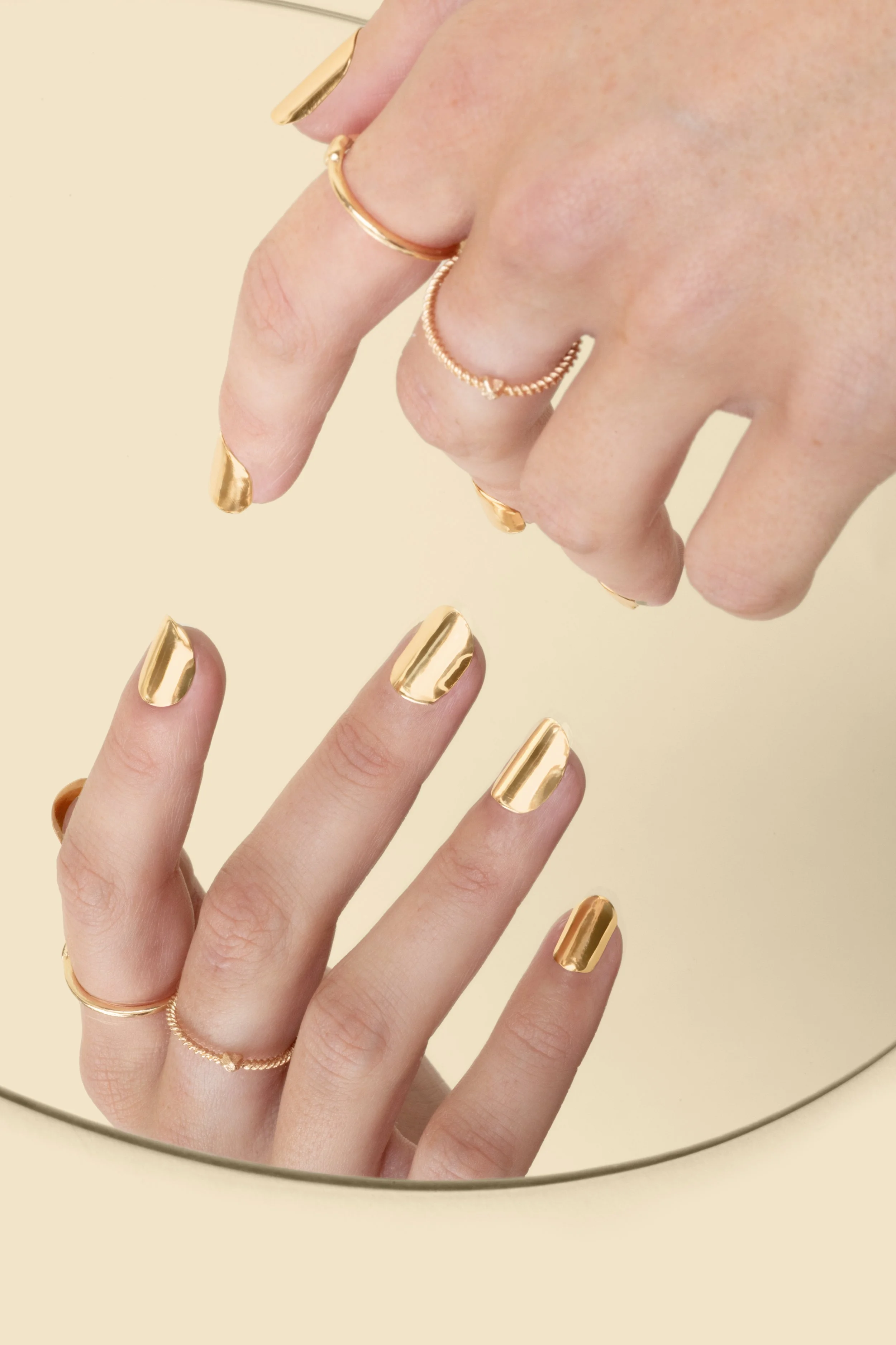 Model wearing 14k yellow gold press-on nails by Stey Gold with mirror finish reflected in mirror