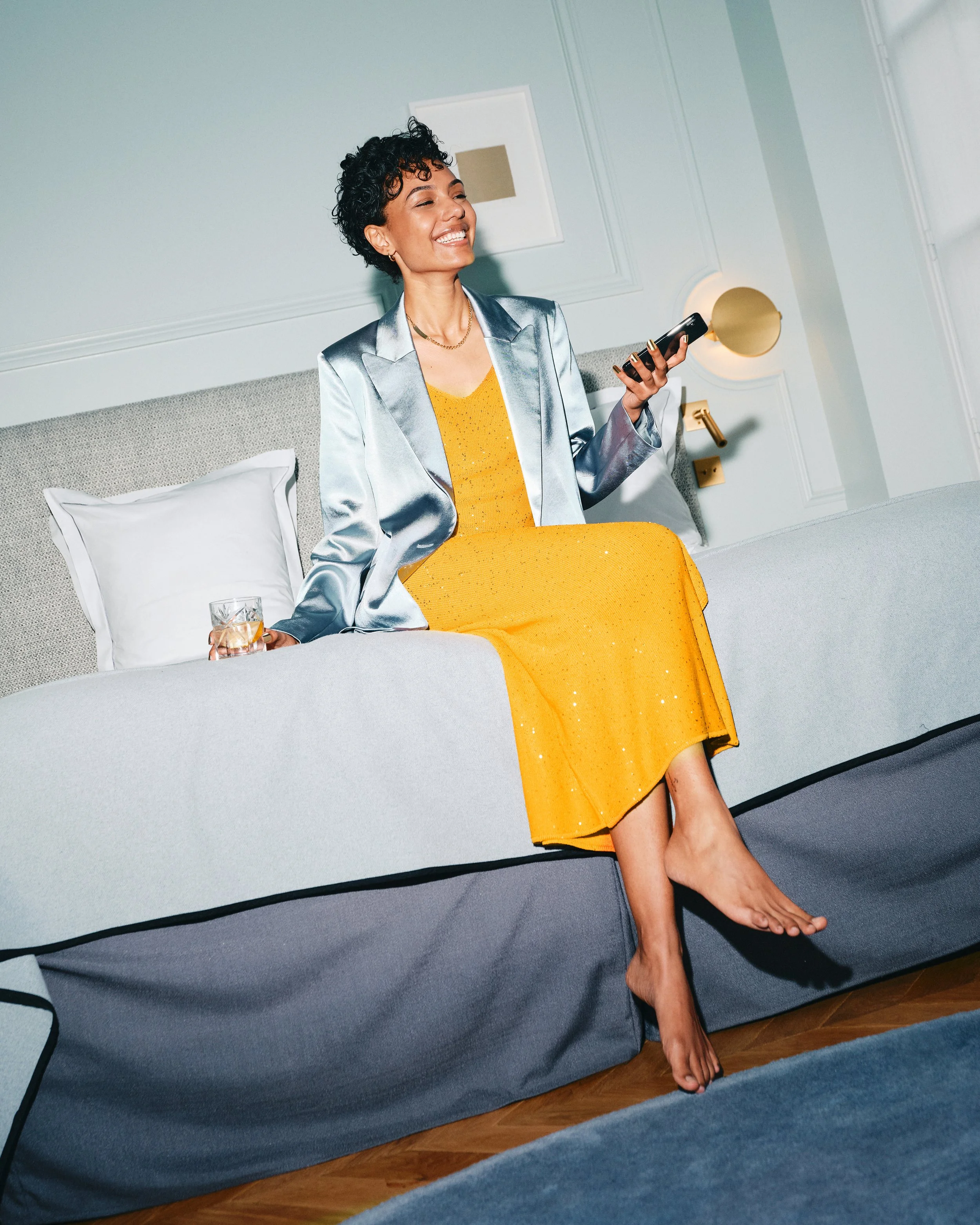 Woman relaxing with a drink wearing 14k gold press-on nails by Stey Gold in a modern living space