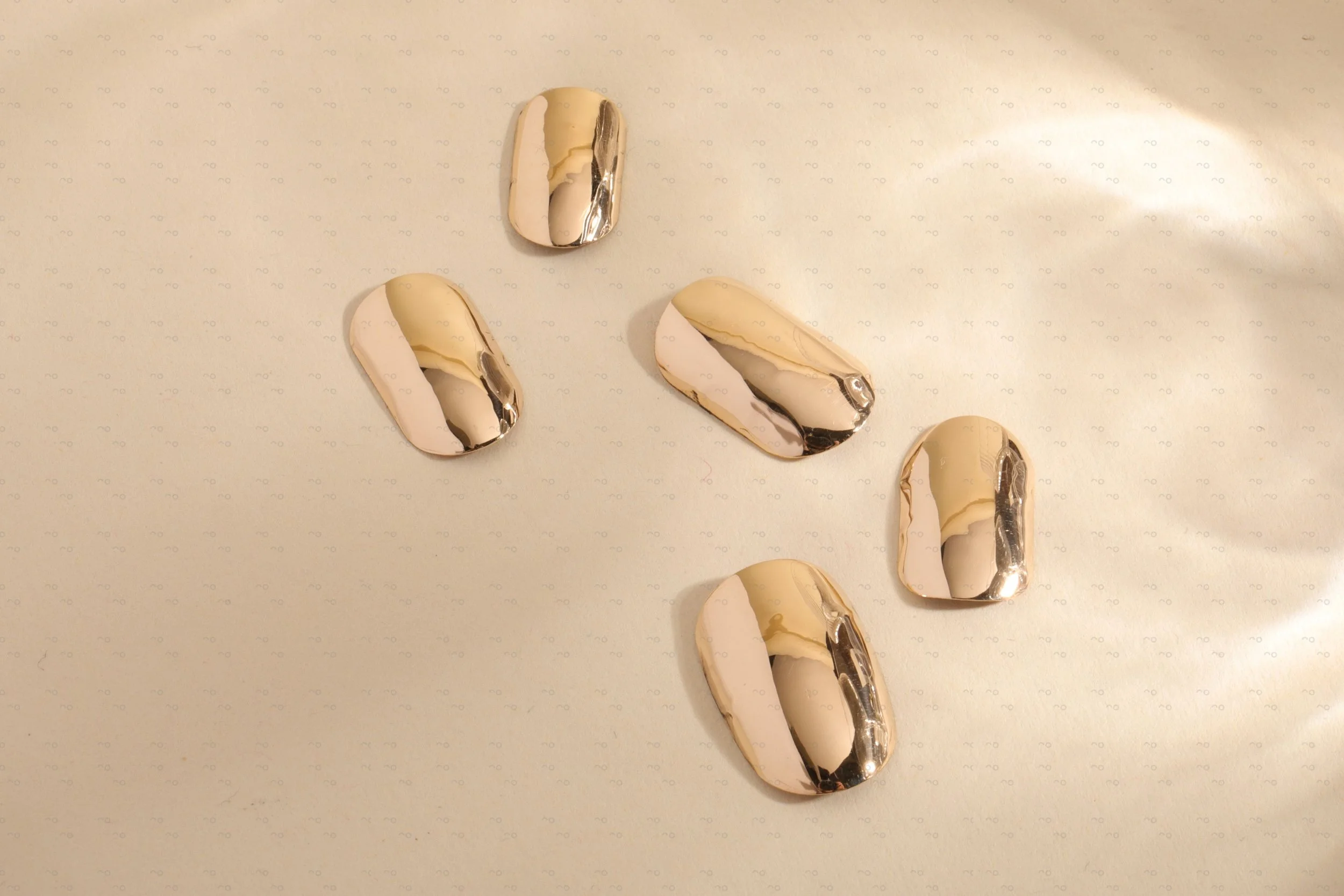 Set of 14k yellow gold press-on nails by Stey Gold with mirror finish arranged on neutral background