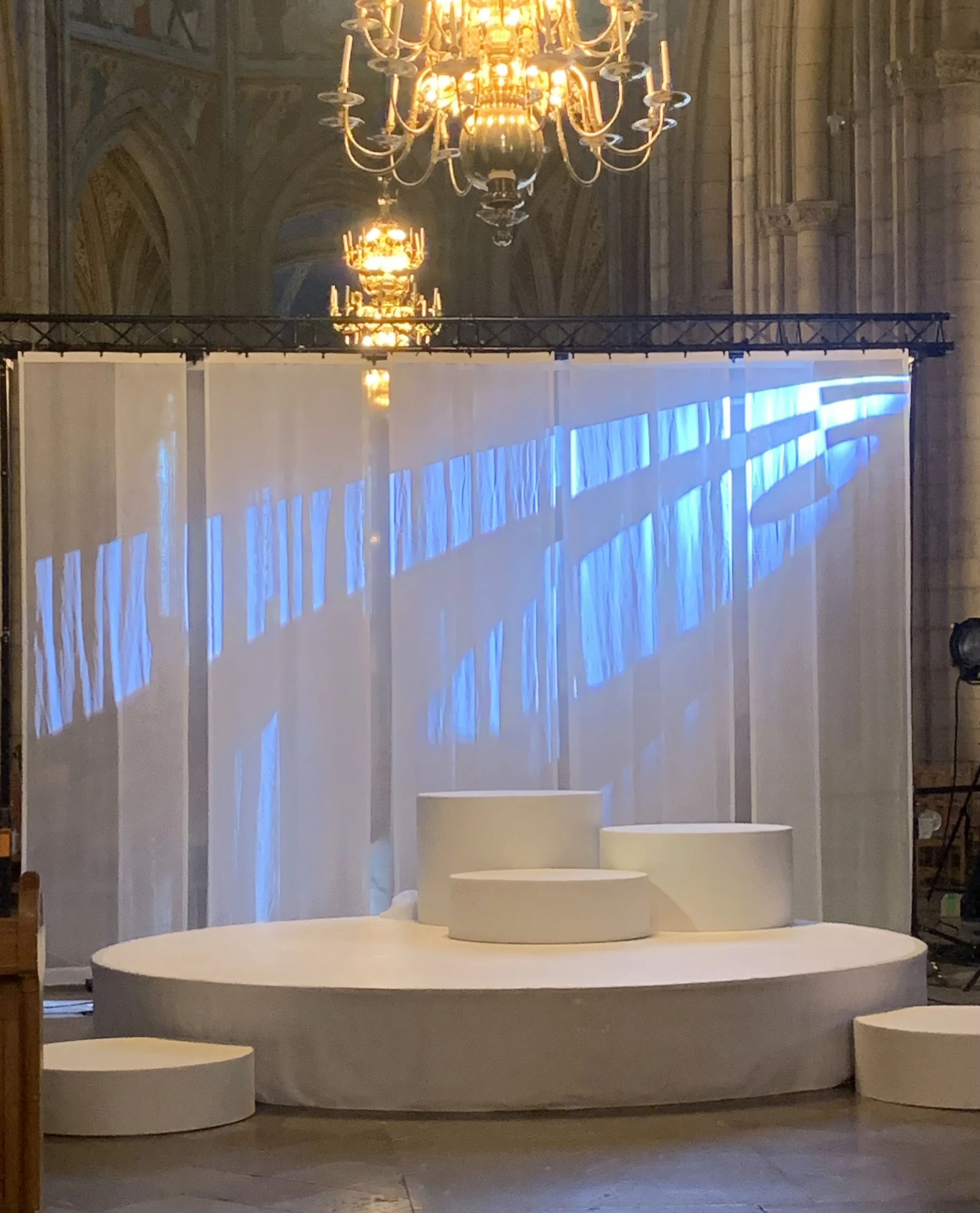 En scen med tre vita, cirkulära podier framför ett vitt skynke. Runt skynket projiceras blå ljus. Hängande lyktor i guld ger ett varmt ljus i lokalen, som verkar vara ett kyrkorum.