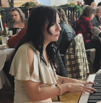 A woman playing a keyboard at a restaurant or cafe with other people in the background.