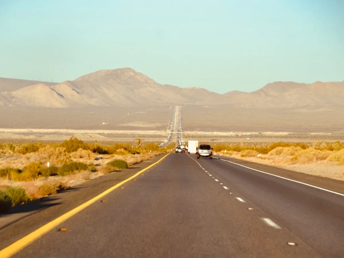 Open desert highway stretching toward distant mountains under a clear blue sky, shot from the driver's perspective