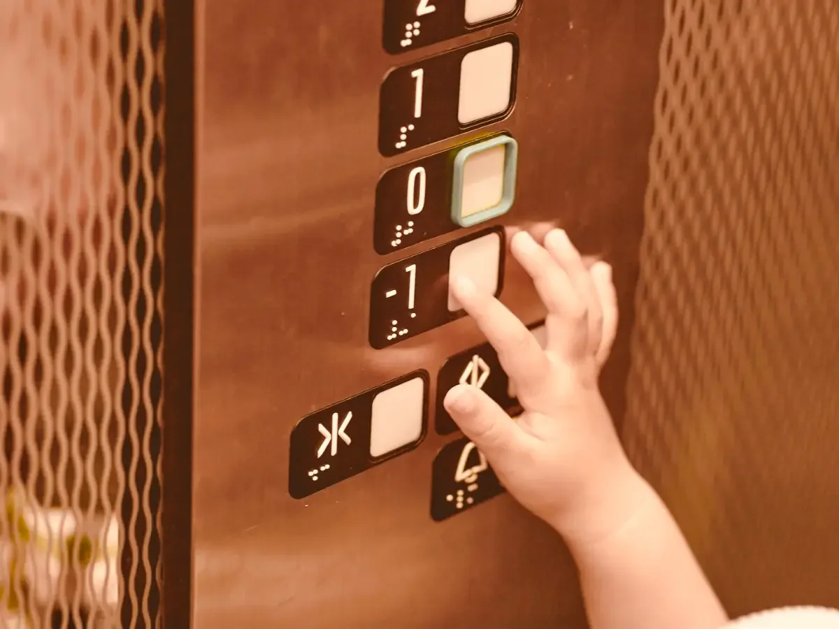 A close-up of a child finger pressing on a vintage elevator floor button. Opening image for She The King's editorial "Why Childhood Vacations Feel Larger Than They Were" on memory, novelty, and the ordinary details a child keeps.
