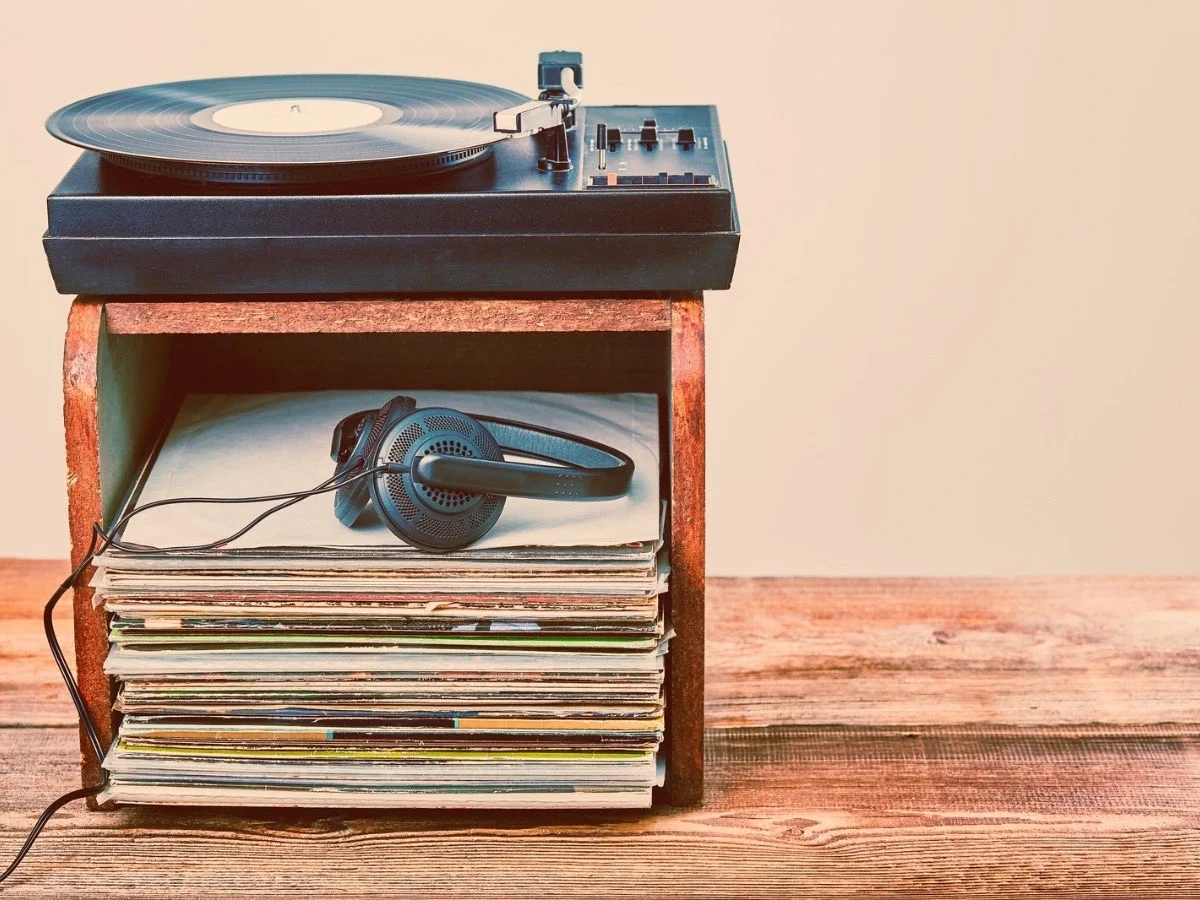 Vintage turntable playing a record, resting atop a stack of vinyl albums with a pair of headphones