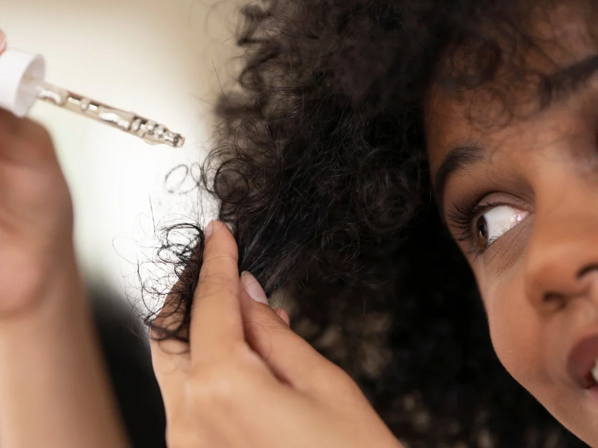 Close-up of a woman watching as oil is applied to her curly natural hair, representing early lessons in caring for and loving natural texture