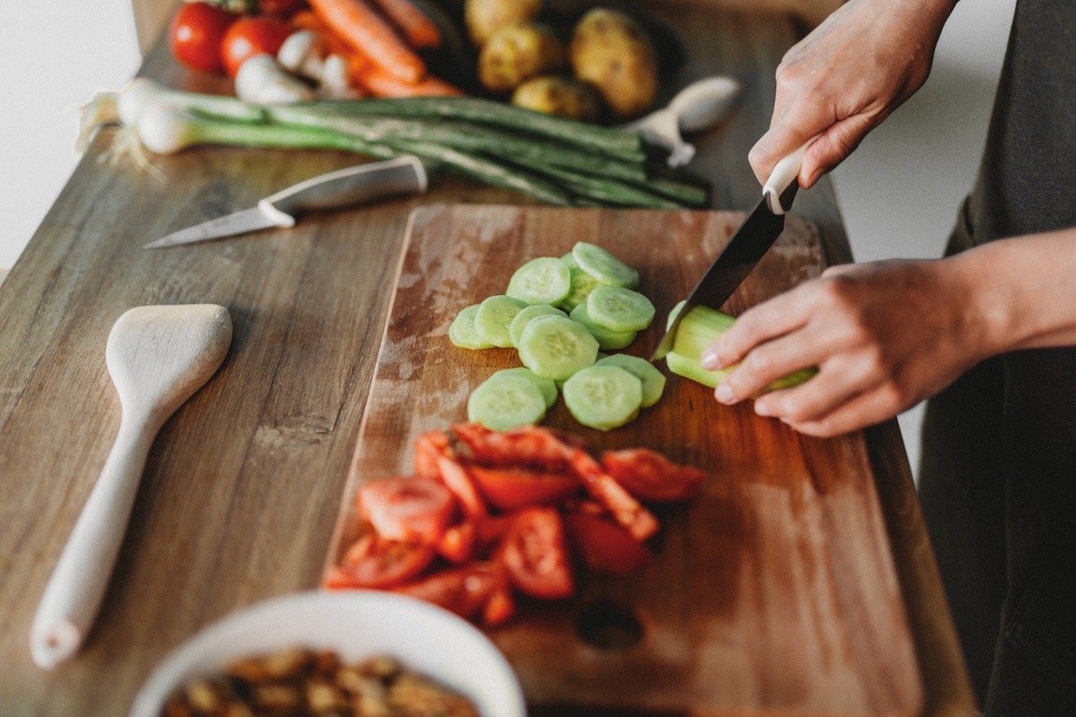 Hands preparing Shirazi salad with cucumbers, tomatoes, and herbs on a wooden cutting board, reflecting Iranian home cooking, cultural memory, and hospitality in The Lion Women of Tehran.
